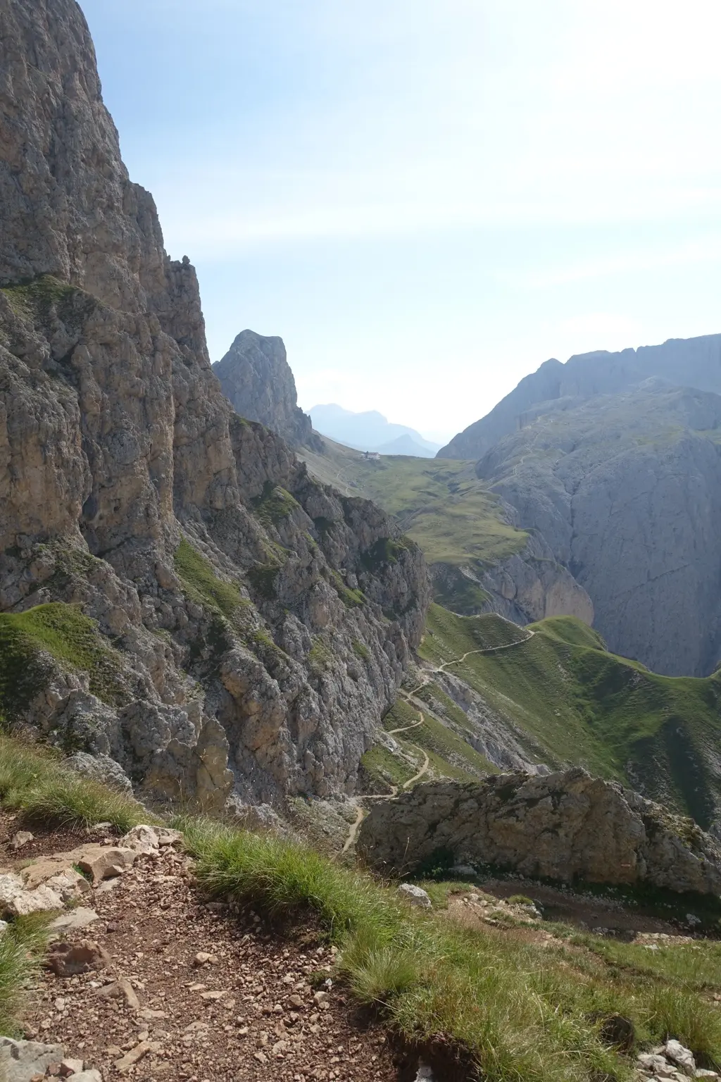 A narrow hiking trail winding between steep rock faces and green slopes in the Dolomites