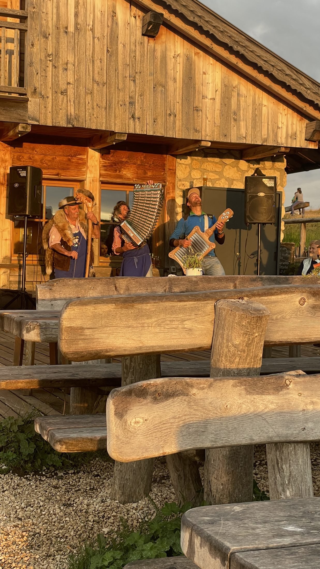 Three musicians playing in golden evening light outside a Dolomites mountain hut