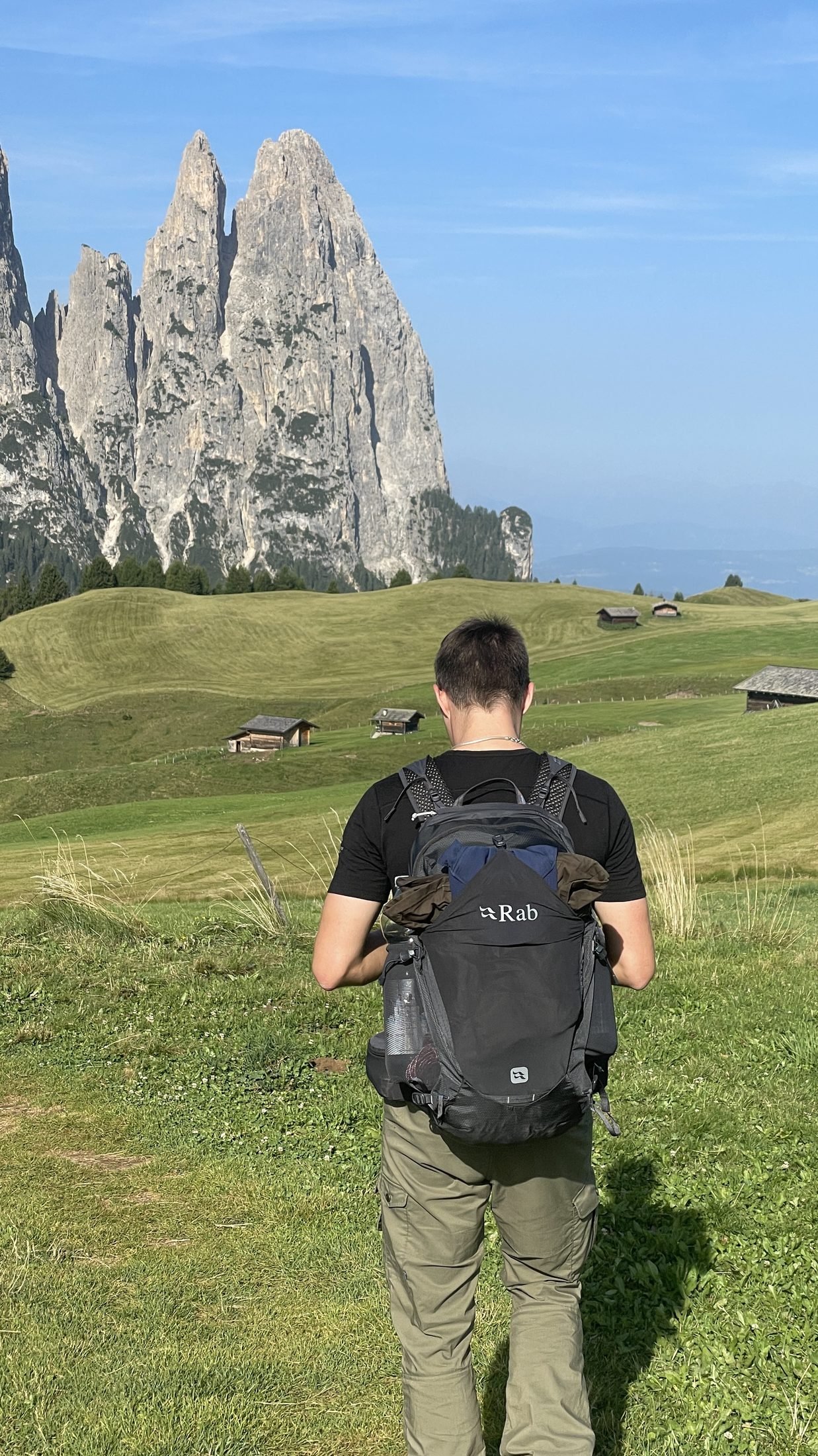 Hiker with a large backpack in front of the rocky Schlern towers on Alpe di Siusi