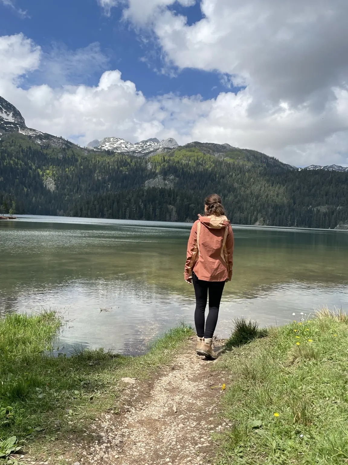 Hiker beside Black Lake beneath forested mountains with patches of snow