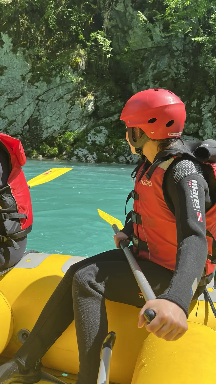 Woman in a red helmet and life jacket inside a yellow raft on the turquoise Tara River