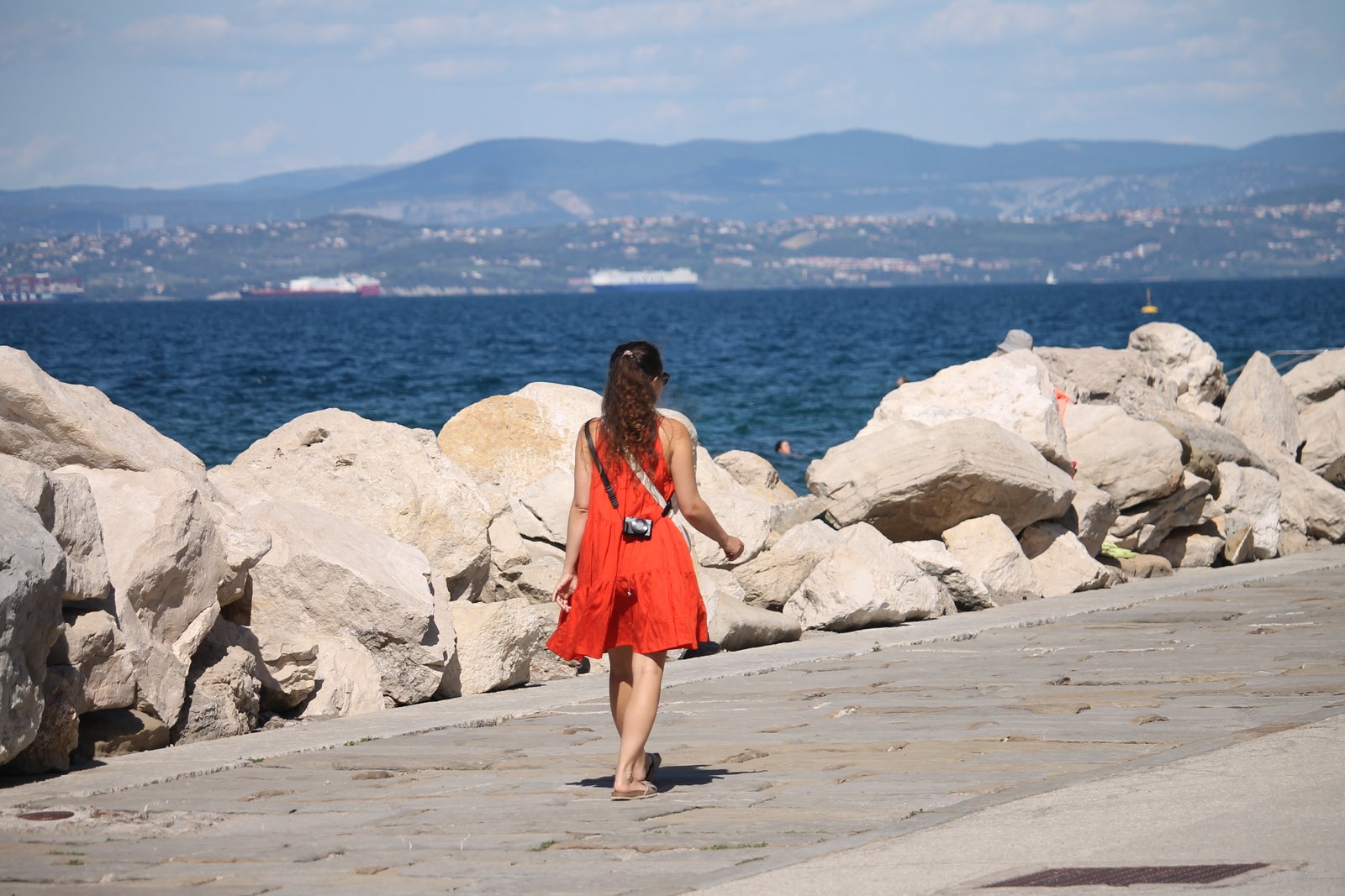 Woman in a red dress on a stone promenade beside the Adriatic Sea