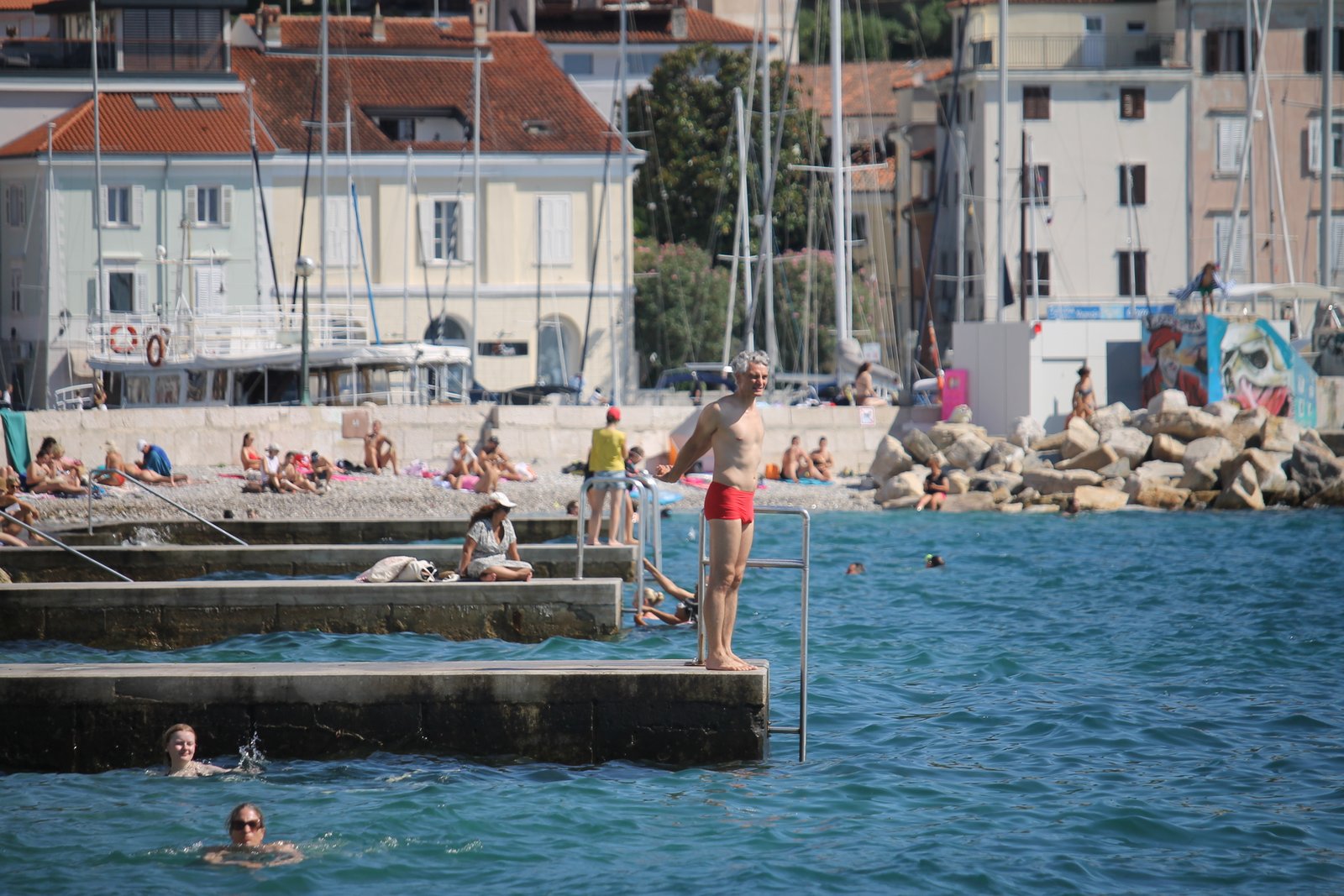 People swimming beside a harbour and waterfront houses on the Slovenian coast