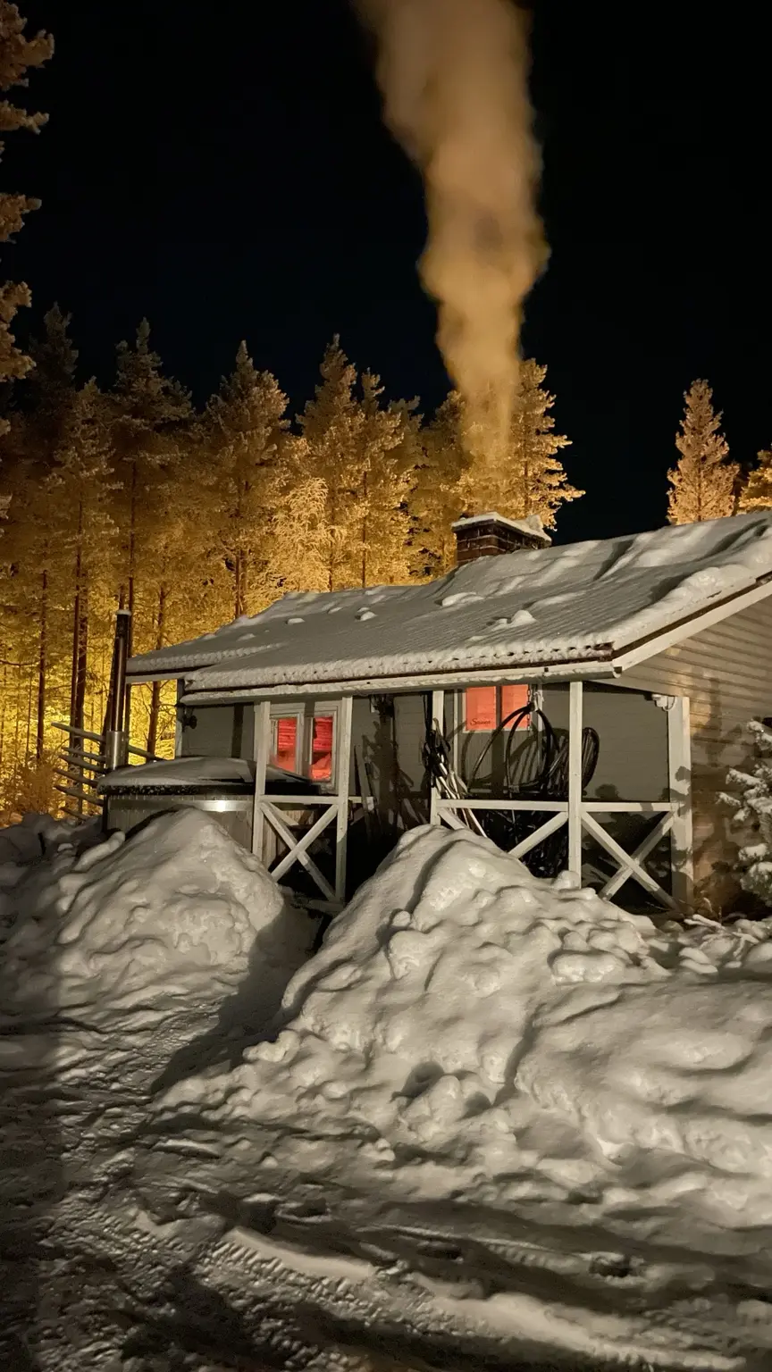 Deeply snow-covered accommodation lit at night in a Finnish Lapland forest