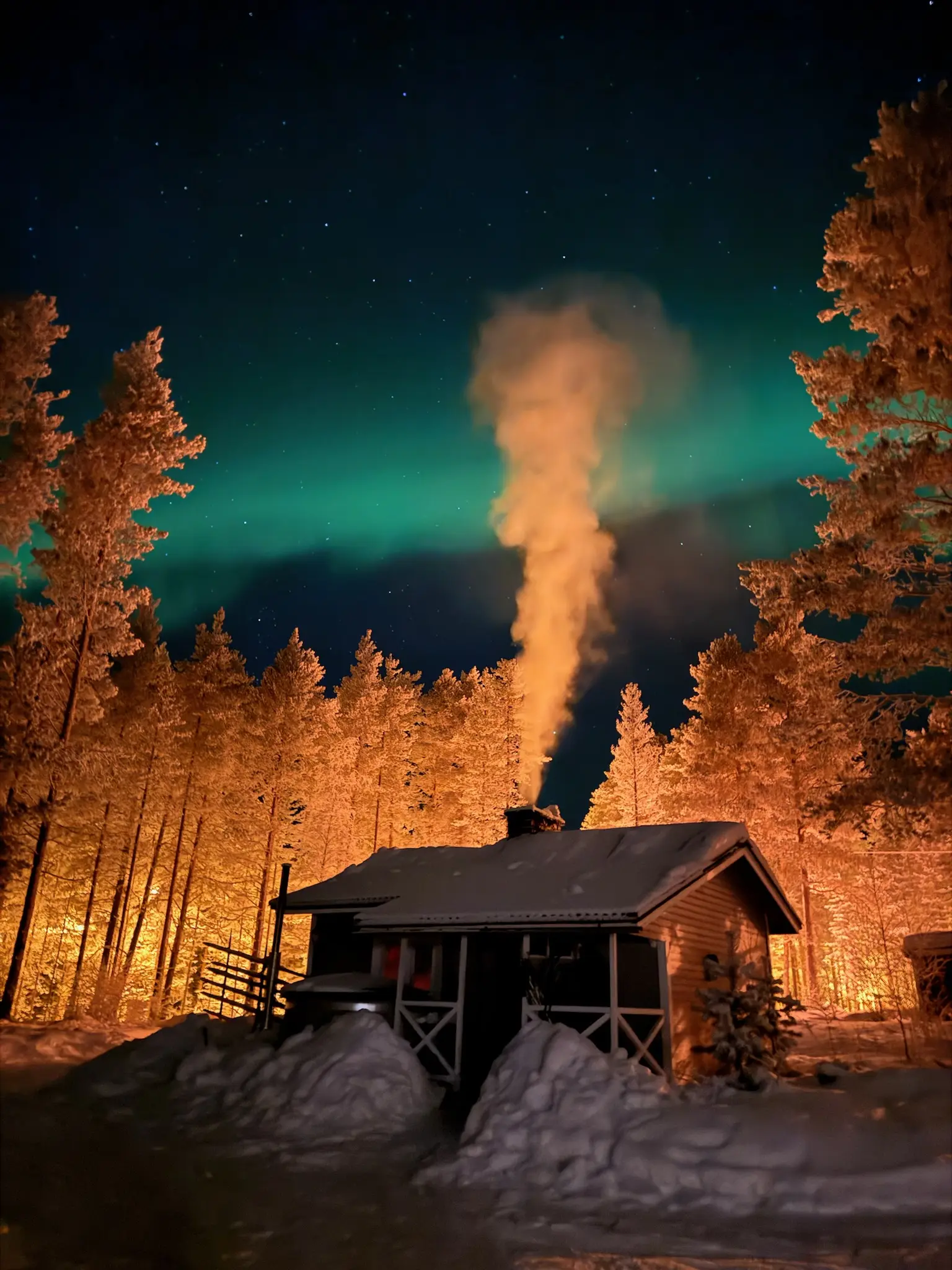 Green northern lights above the separate sauna building in a deeply snow-covered forest