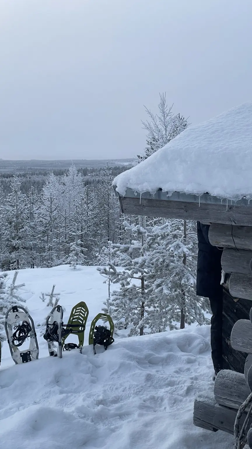 Snowshoes standing outside a deeply snow-covered log cabin in Finnish Lapland