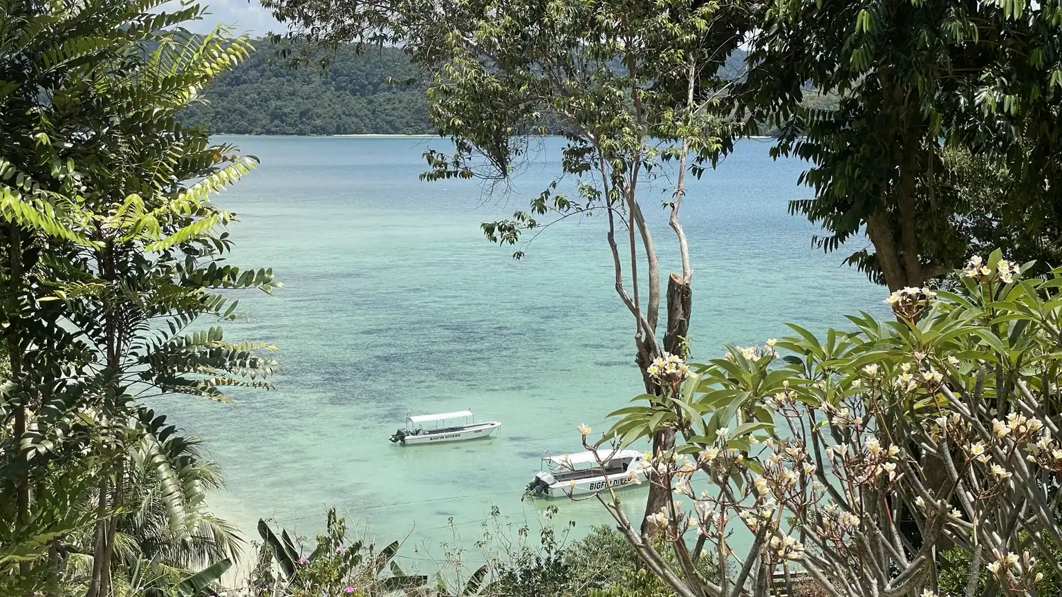 A turquoise bay in Borneo framed by tropical trees, with two small boats on the water